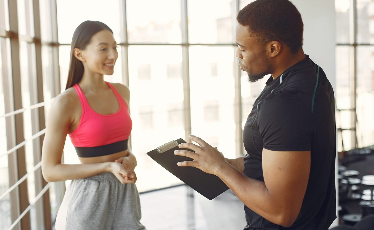 Handsome black man in a gym. Sportspeople in a sportswear. Woman talking with coach.