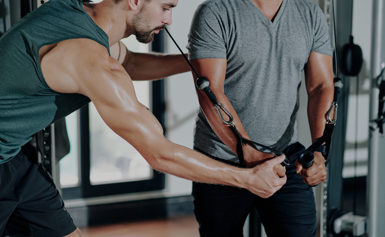 portrait-recadre-d-un-entraineur-de-fitness-expliquant-au-client-comment-faire-de-l-exercice-dans-une-machine-de-croisement-de-cables